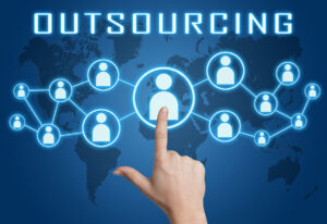 A hand pointing towards a central figure in a digital network of connected people, symbolizing the concept of outsourcing. The word 'Outsourcing' is displayed at the top, with a world map in the background highlighting global connections