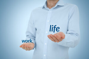 The image shows a person wearing a light blue shirt, with their hands extended in front of them. The word "work" appears on their left hand, and the word "life" appears on their right hand. The imagery suggests the concept of balancing work and life responsibilities, highlighting the importance of work-life balance. The background is a soft blue, adding a calm and balanced visual tone to the image.