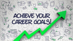 The image shows a brick wall with the phrase "Achieve Your Career Goals!" written on it. Surrounding the text are various illustrations of office supplies, gadgets, and work-related objects, with a bold green arrow pointing upward, symbolizing growth, success, and progress. This visual would work well in content focused on career growth, productivity, or goal achievement, reinforcing the message of upward momentum and reaching new heights in one’s professional life. Would you like to use this image as a part of a project or incorporate it into your blog post?