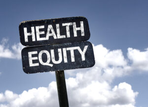 A wooden signpost with two arrows reading "HEALTH" and "EQUITY" against a backdrop of a clear blue sky with scattered clouds. The sign appears aged, emphasizing the enduring importance of health equity in public discourse.