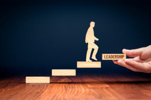 A wooden figure climbs stairs labeled "Leadership," symbolizing growth, personal development, and guidance toward self-leadership and success.
