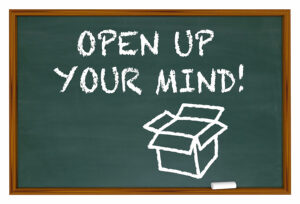 OPEN UP YOUR MIND!" written in white chalk with a simple, open cardboard box drawn underneath, symbolizing thinking outside the box and openness to new ideas