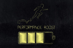 Illustration on a blackboard background showing a yellow chalk-style drawing of a battery charging and a person energetically leaping forward above the words “Performance Boost,” symbolizing increased energy, motivation, and productivity.